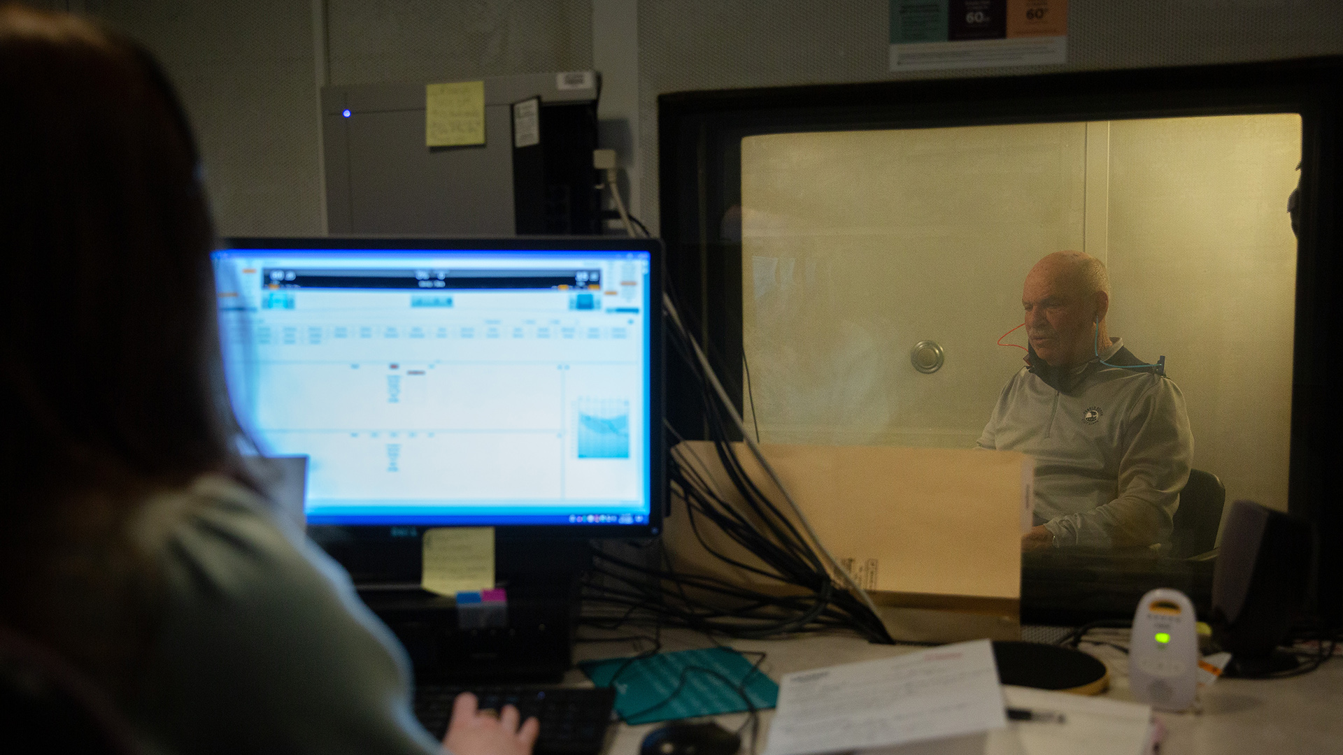 A patient sits behind a glass window at the Speech and Hearing Clinic.